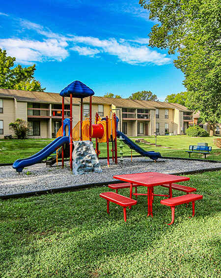 A playground with a red table and benches in front of apartment buildings.