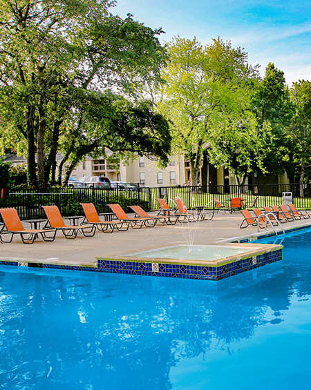 A pool surrounded by trees and chairs.