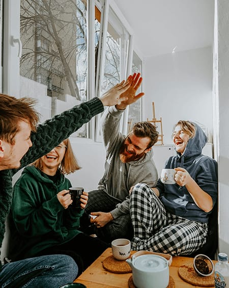 Four people sitting on a windowsill, one with a green sweater raising their hand.