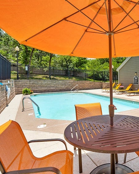 a pool with an orange umbrella and a table with chairs