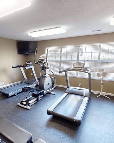 A gym with a treadmill, elliptical trainer, and a fan.