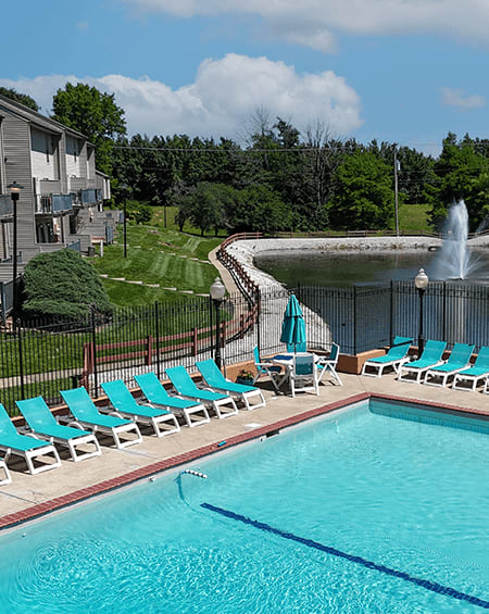 A pool with a waterfall and chairs around it.