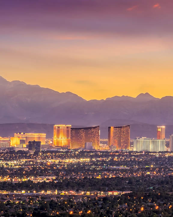 A cityscape with a mountain range in the background and a lit up tower in the middle.