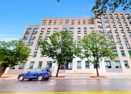 A blue car is parked on the street in front of a multi-story building.