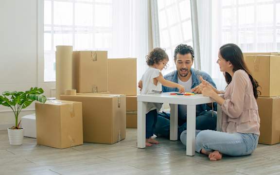 A family is sitting on the floor surrounded by moving boxes.