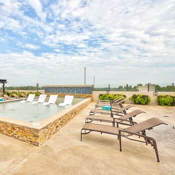 The pool on the roof of the Edge at Midtown Apartment Homes with chairs around it and white chairs in the pool. 