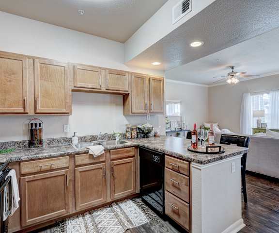 A kitchen with black appliances, marble countertops, and wooden cabinets with decorations at Lincoln at Central Park Apartment Homes. 