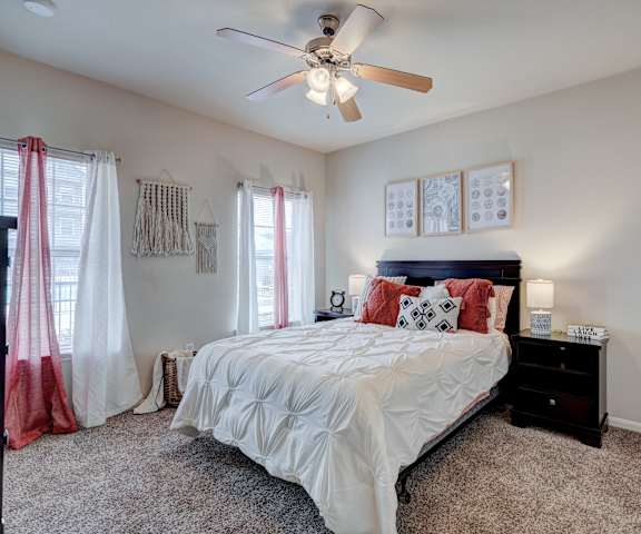 A bedroom with a queen-size bed, a dresser, decorations, window, and nightstands at Lincoln at Central Park Apartment Homes. 