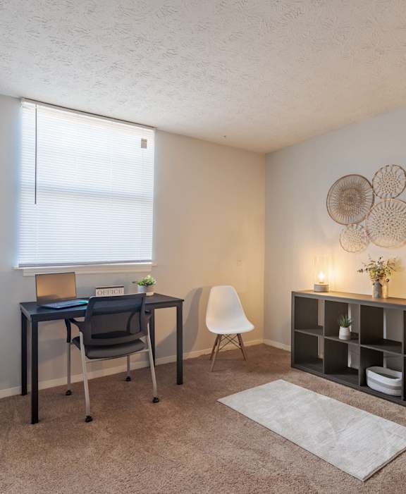 A room with a desk, chair, and shelves with decorative items.