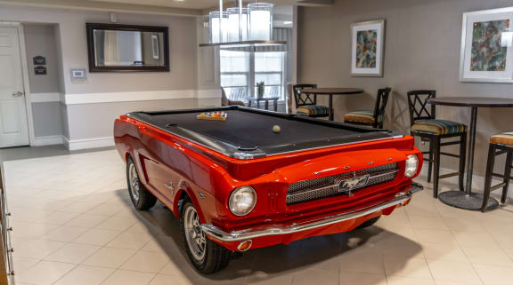 a pool table with a red car in the middle of the room