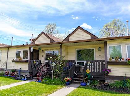 a house with yellow siding and a porch with potted plants and flowers