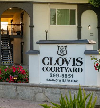 The entrance to Clovis Courtyard with a sign and flowers.