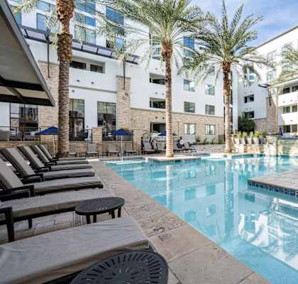 A pool surrounded by palm trees and lounge chairs.