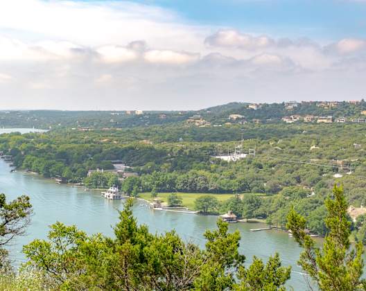 A river flows through a lush green valley with boats and houses along the riverbanks.