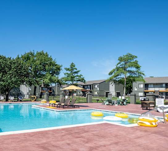 a swimming pool at an apartment complex with chairs and umbrellas
