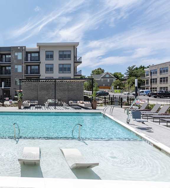 a swimming pool with lounge chairs in front of an apartment building