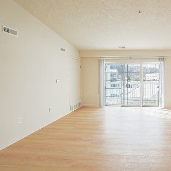 A large empty room with wooden floors and a glass door leading outside.