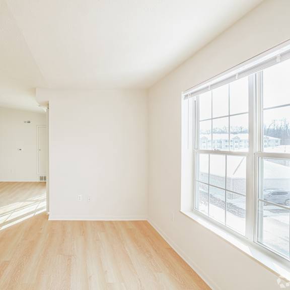 A large empty room with wooden floors and a window overlooking a snowy landscape.