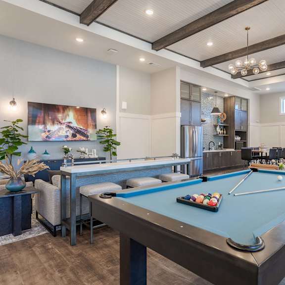 A pool table is in the middle of a room with a bar and a painting on the wall.