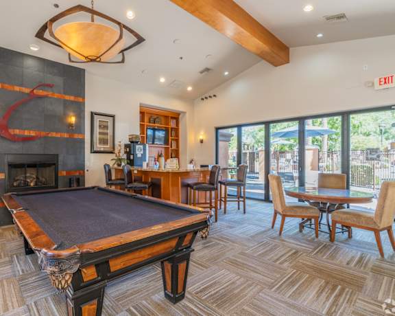 A pool table is in the middle of a room with a fireplace and a bar.