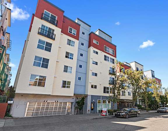 an apartment building with a parking lot in the foreground and a blue sky in the background at Promenade at the Park Apartment Homes in Seattle, WA