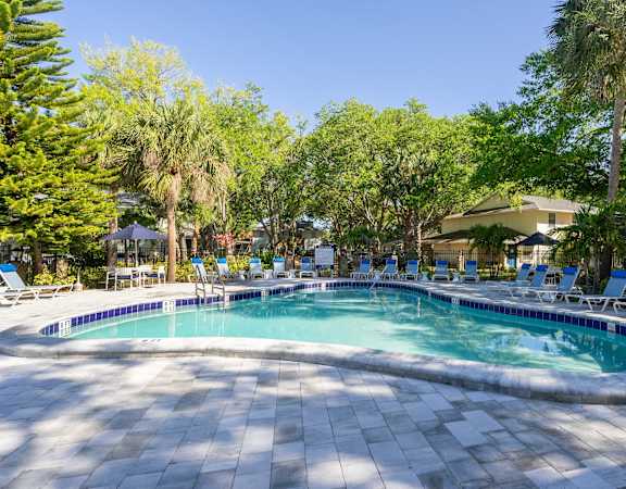 a swimming pool with chaise lounge chairs and trees in the background