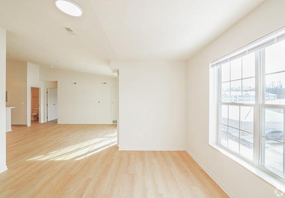 A large empty room with wooden floors and a window overlooking a snowy landscape.