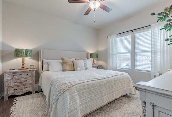 Bedroom with a large bed, curtained windows, and a ceiling fan.