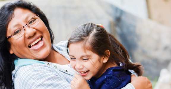 A woman with glasses is hugging a young girl.