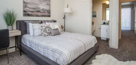 A bedroom with a bed, a desk, a chair, a ceiling fan, and a painting on the wall. at Liberty Square Apartments - Saltlake City, UT Apartments, Saltlake City, Utah