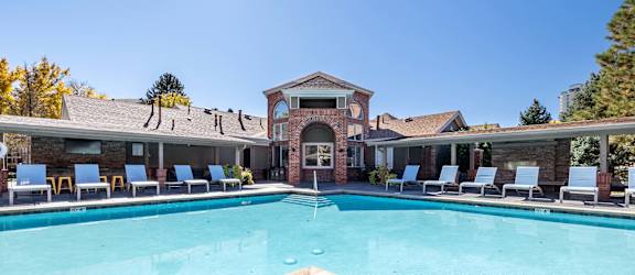 A large swimming pool in front of a building with lounge chairs around it.