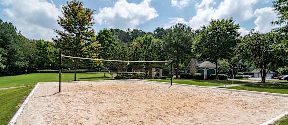 a sand volleyball court in a park with trees and a house