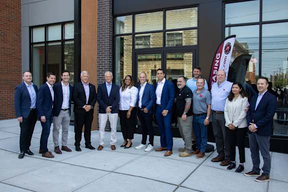 A group of people in business attire stand in front of a building with a glass door.