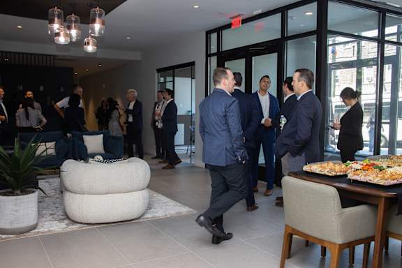 A group of people in suits are gathered in a room with a pizza on a table.