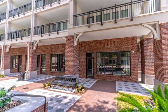 A brick building with a balcony and a bench in front.