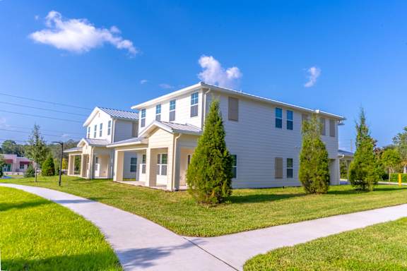A white house with a grey roof and a green lawn in front.