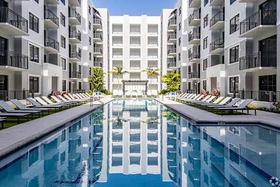 A large white apartment complex with a pool in the middle at Leena Plantation in Plantation, FL