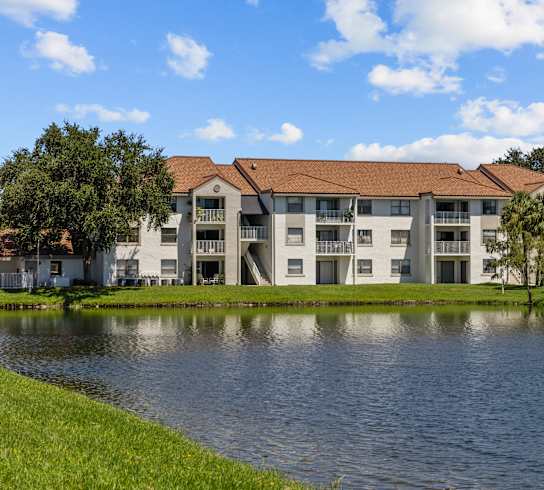 A large building with a red roof is situated next to a body of water.