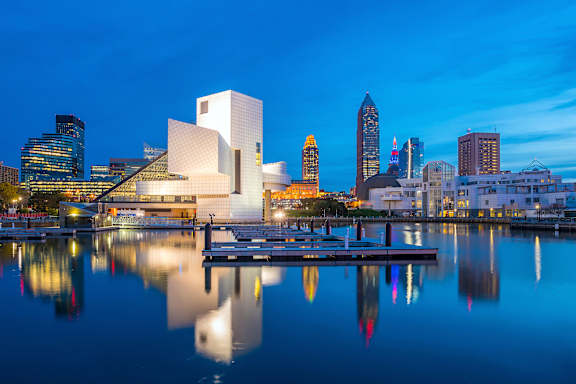 The image shows a serene cityscape with a building that resembles a white cube in the foreground, reflecting on the calm water surface.