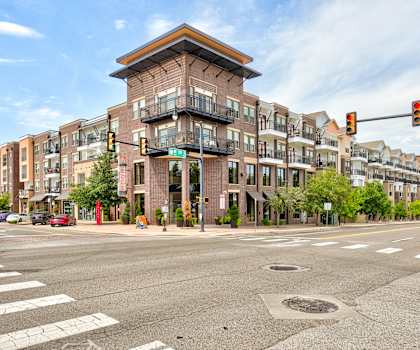 The street view from a city black of the brick apartment building with trees in the sidewalk in front of the building at the Edge at Midtown Apartment Homes. 