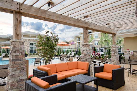 Outdoor lounge with orange cushioned seating under a pergola near the pool  at Residences at Prairiefire Apartment Homes, Overland Park, KS, 66223