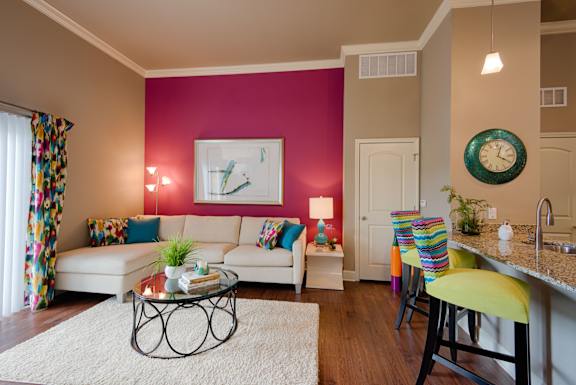 Stylish living room at Residences at Prairiefire featuring a bold magenta accent wall, sectional sofa, and breakfast bar with colorful seating. at Residences at Prairiefire Apartment Homes, Overland P