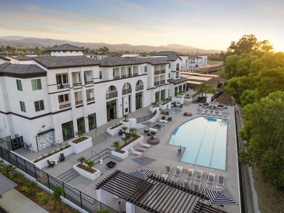 A large white building with a pool in the foreground and a mountain in the background. at The Venue at Orange Apartments, California