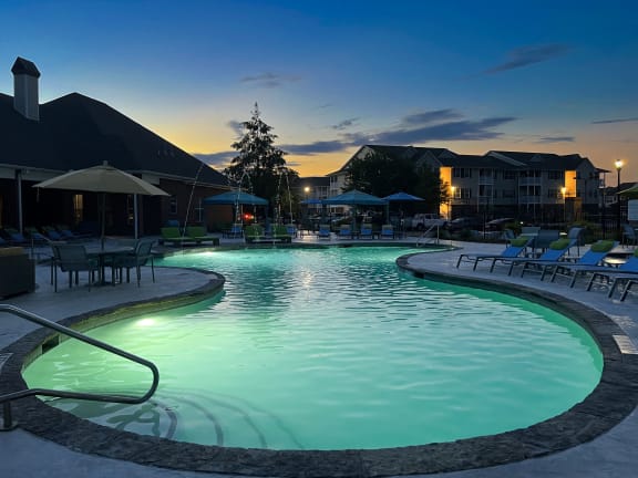 a swimming pool with chaise lounge chairs and a pool house in the background at The Madison Apartment Homes in Tyler, TX 75703