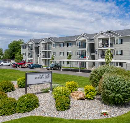 an apartment building with a sign and landscaping in front of it