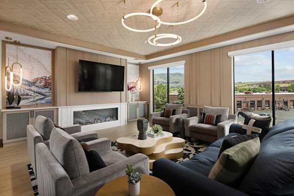 A modern living room with a large grey sofa, a wooden coffee table, and a flat-screen TV mounted on the wall.