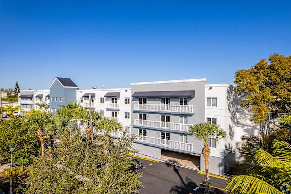 A white building with a balcony is surrounded by trees.