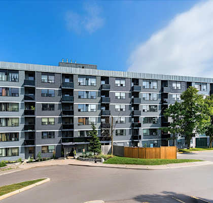 A large grey apartment building with a parking lot in front.