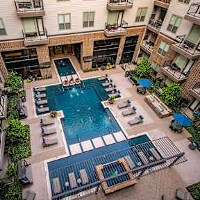 A large swimming pool surrounded by lounge chairs and umbrellas in a courtyard surrounded by apartment buildings.