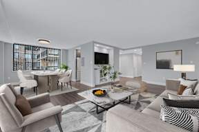 A modern living room with a large grey sofa, a coffee table, and a dining table with chairs.